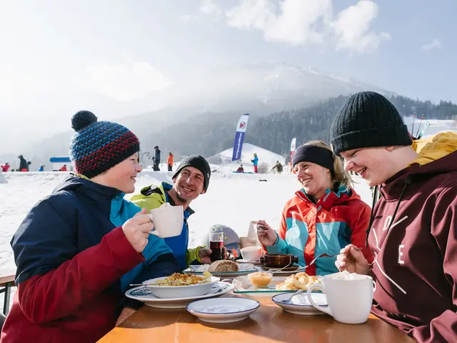 Eine Familie bei der Einkehr an der Skipiste, im Hintergrund eine verschneite Landschaft.