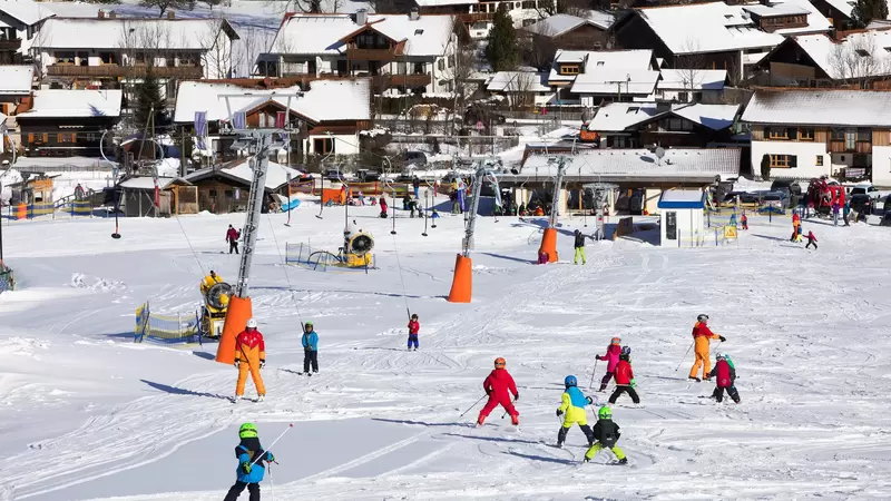 Kinder fahren die Skipiste hinunter, neben ihnen ist ein Tellerlift zu sehen.